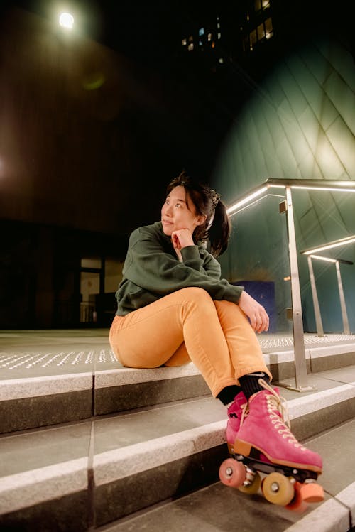 Pensive young Asian woman resting on steps in city after rollerskating