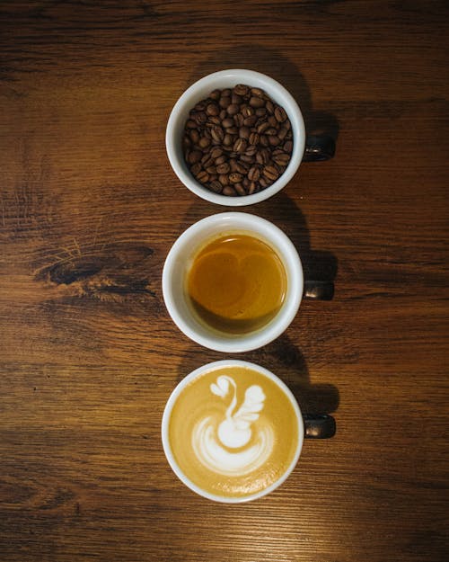 Top view arrangement of cups with fresh cappuccino espresso and coffee beans placed in row on wooden table