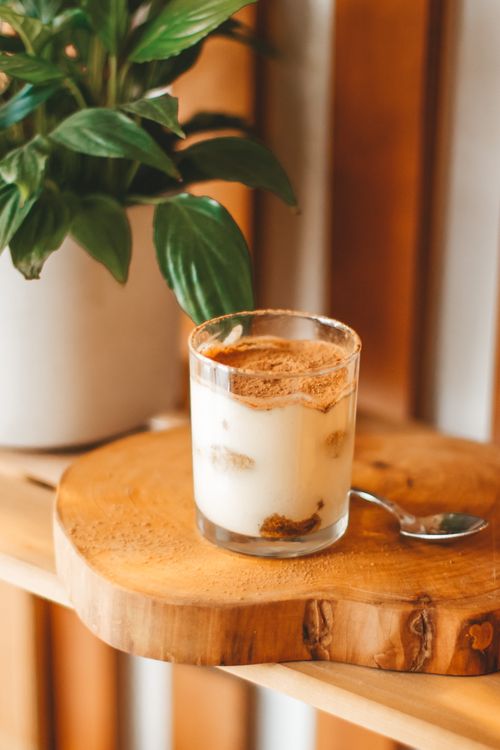 Free Glass of fresh yummy yogurt and teaspoon served on wooden board on shelf near lush houseplant Stock Photo