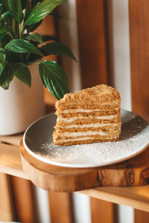 Free Slice tasty sweet Napoleon cake placed on gray ceramic plate on wooden table near green potted plant on blurred background Stock Photo