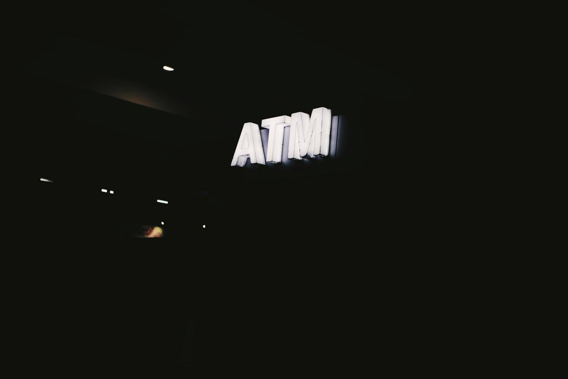 Glowing bright white ATM signboard hanging on wall in darkness in night time