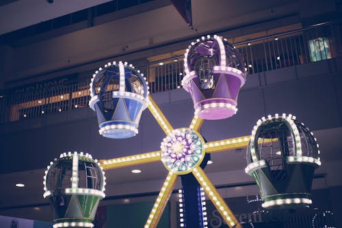 From below of small colorful Ferris wheel with bright lights placed in amusement park