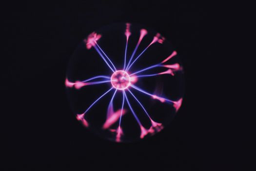Transparent glass plasma ball with bright neon luminous against dark background in room