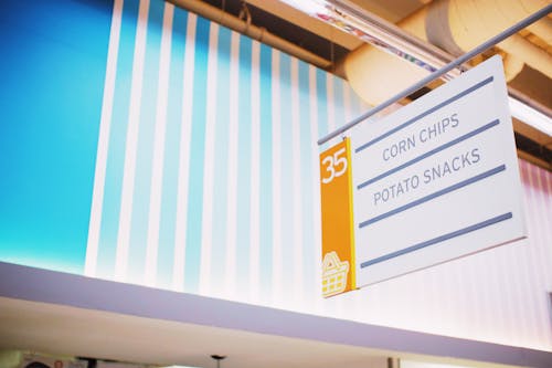 Free From below of signboard with inscription Corn chips Potato snacks hanging under ceiling in contemporary supermarket Stock Photo