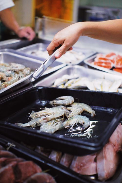 Free Crop unrecognizable seller using metal tongs for taking fresh shrimps in local market in daytime Stock Photo