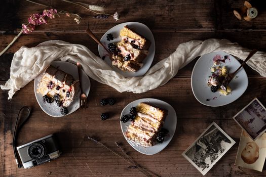 A rustic flatlay of blackberry cake slices on plates with vintage elements and a retro camera.