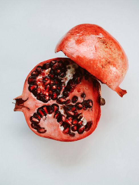 Vibrant sliced pomegranate showcasing seeds on a clean white surface, highlighting its fresh and colorful appeal.