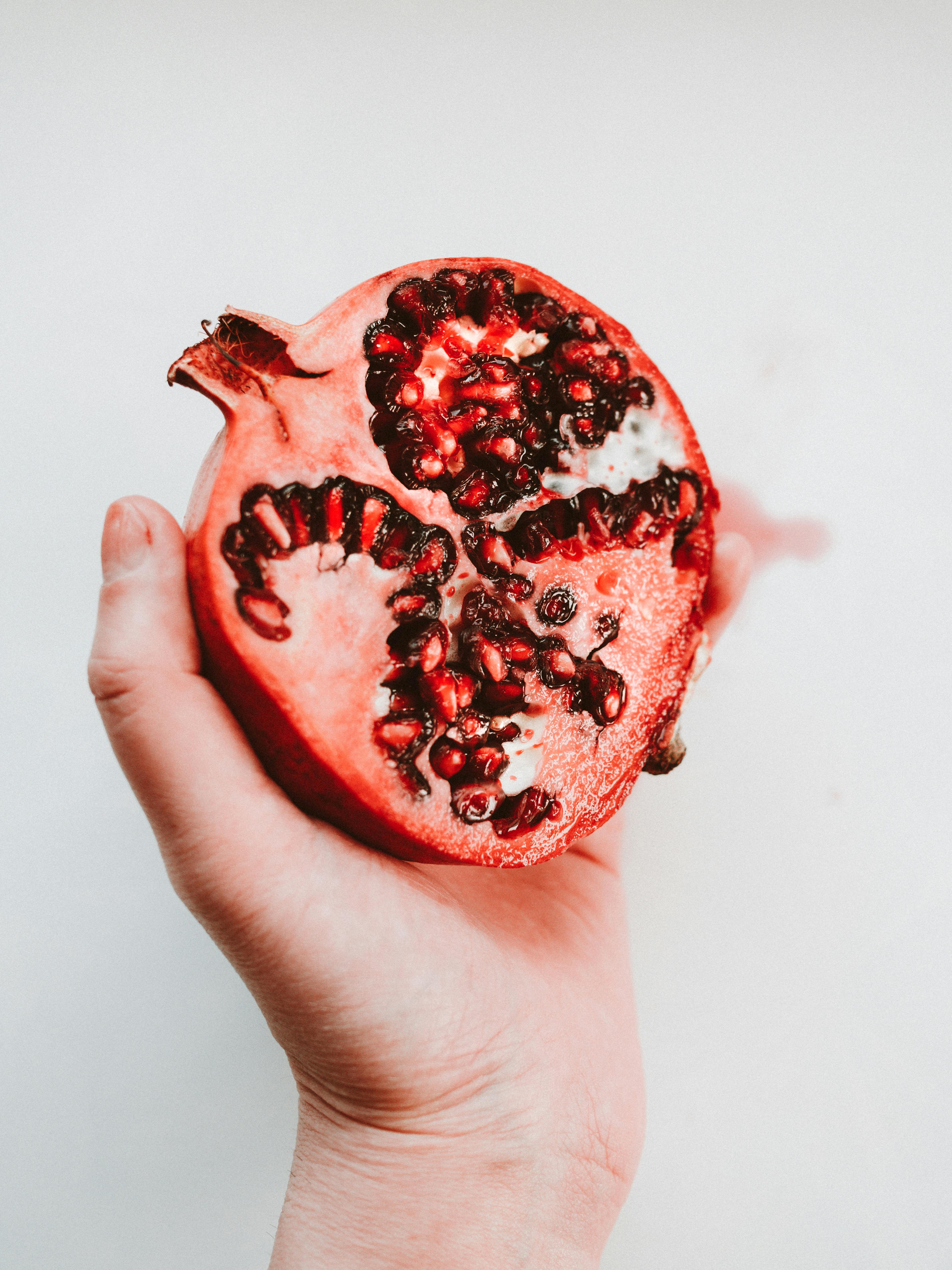 Fresh half pomegranate held in a hand against white background, showcasing vibrant seeds.