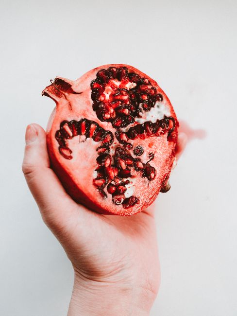 Fresh half pomegranate held in a hand against white background, showcasing vibrant seeds.