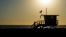 日落时分，一座救生员小屋的剪影与美国国旗一同俯瞰着大海