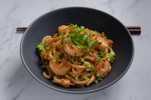 A mouth-watering dish of shrimp udon noodles garnished with scallions and chili flakes.