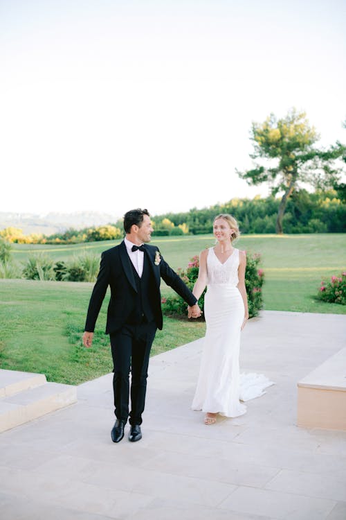 Man in Black Suit Holding Hands with Woman in White Dress