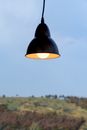 Contemporary lamp with light bulb glowing on background of sky in countryside in evening