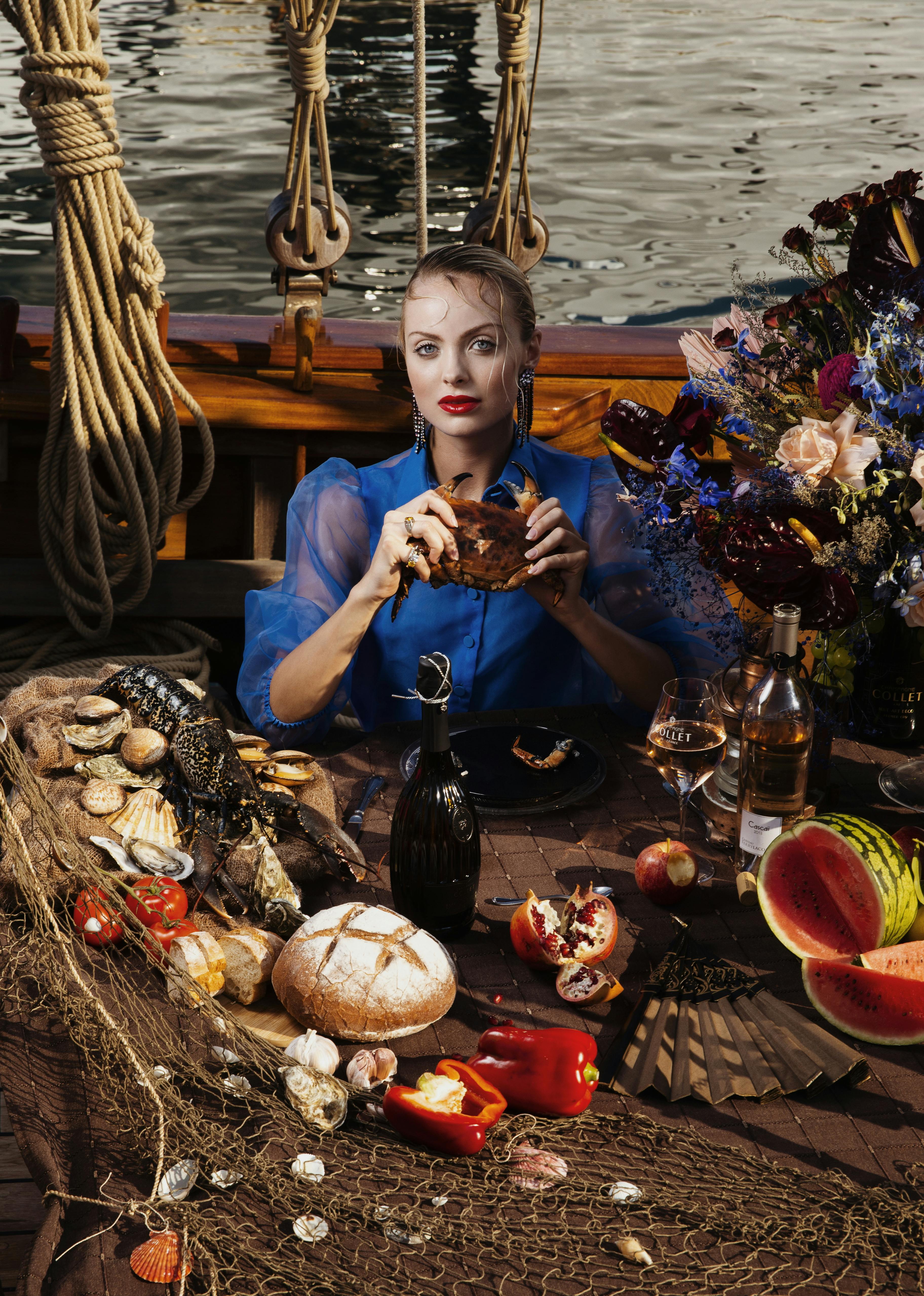 A fashionable woman enjoys a luxurious seafood feast on a beautifully set table aboard a ship.