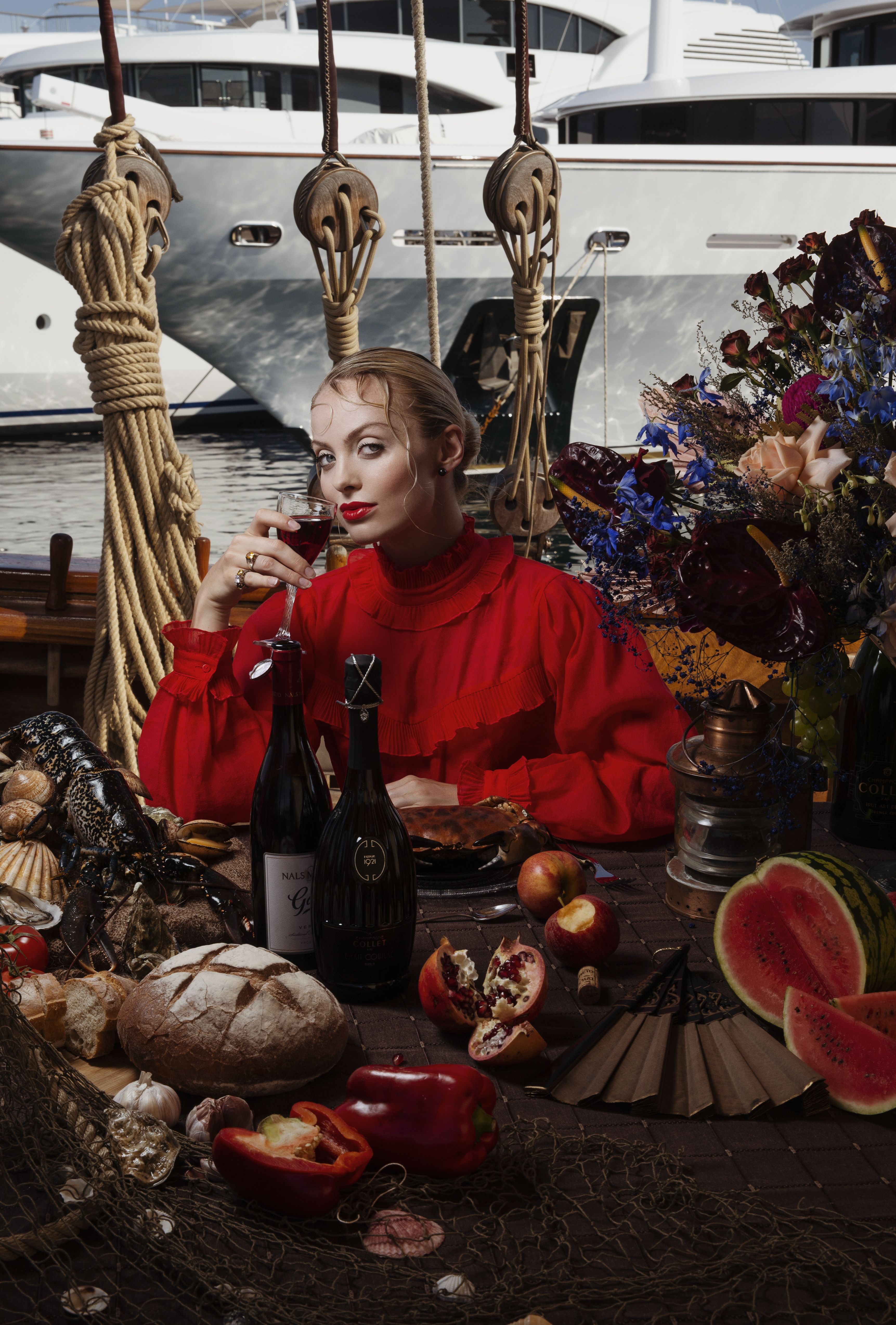 Glamorous woman in red enjoying wine on a yacht with luxurious food spread.