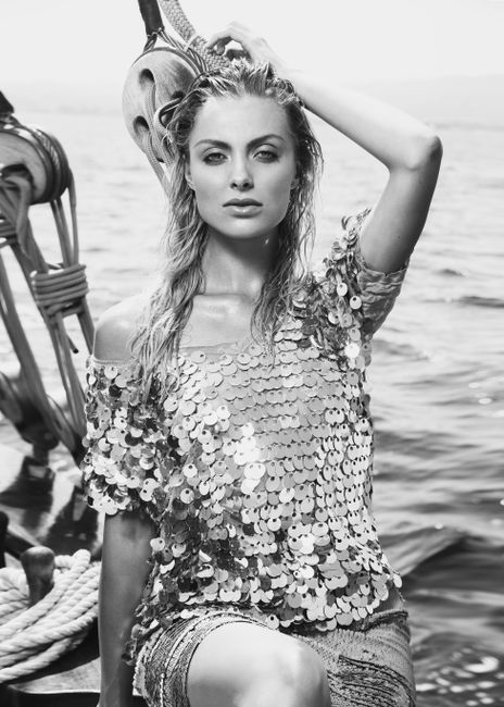 Black and white of charming female in trendy outfit looking at camera while sitting on yacht near rippling sea during trip