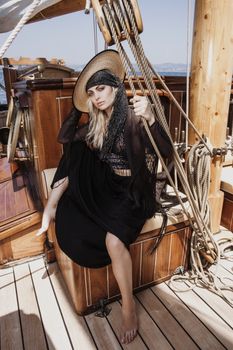Fashion model posing elegantly on a wooden sailboat deck, exuding style and grace.