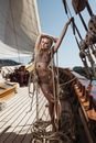 Full body of gorgeous female in swimsuit standing on wooden deck of yacht with ropes during cruise on summer day