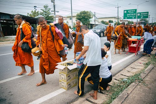 People on the Side of the Road Giving Water to Walking Monks 