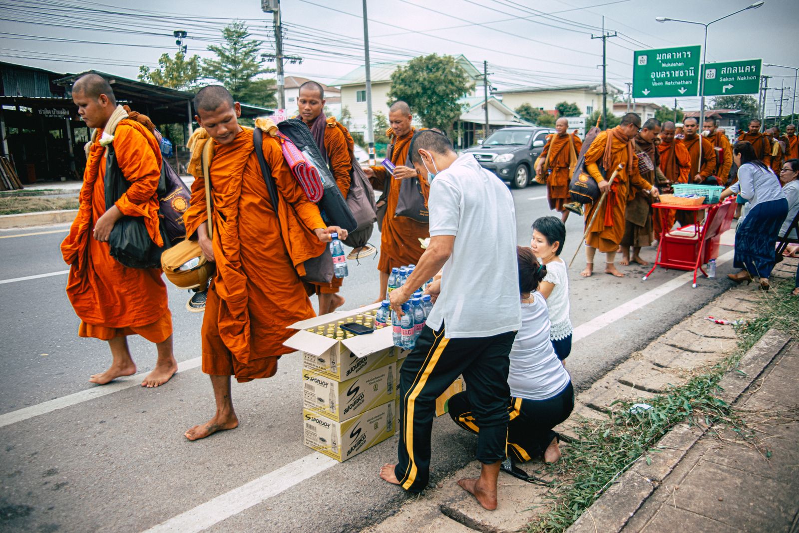 Residents on a roadside passing water to monks walking for alms