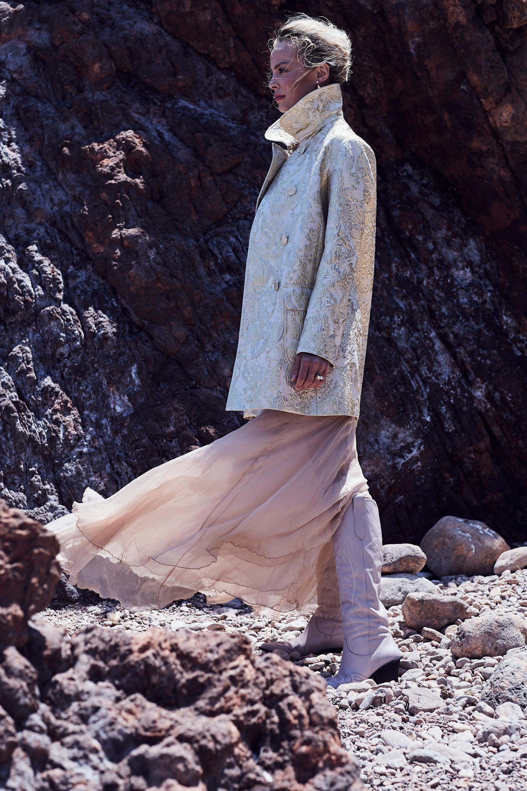 A stylish woman in a textured coat and skirt posed dramatically against rugged rocks.