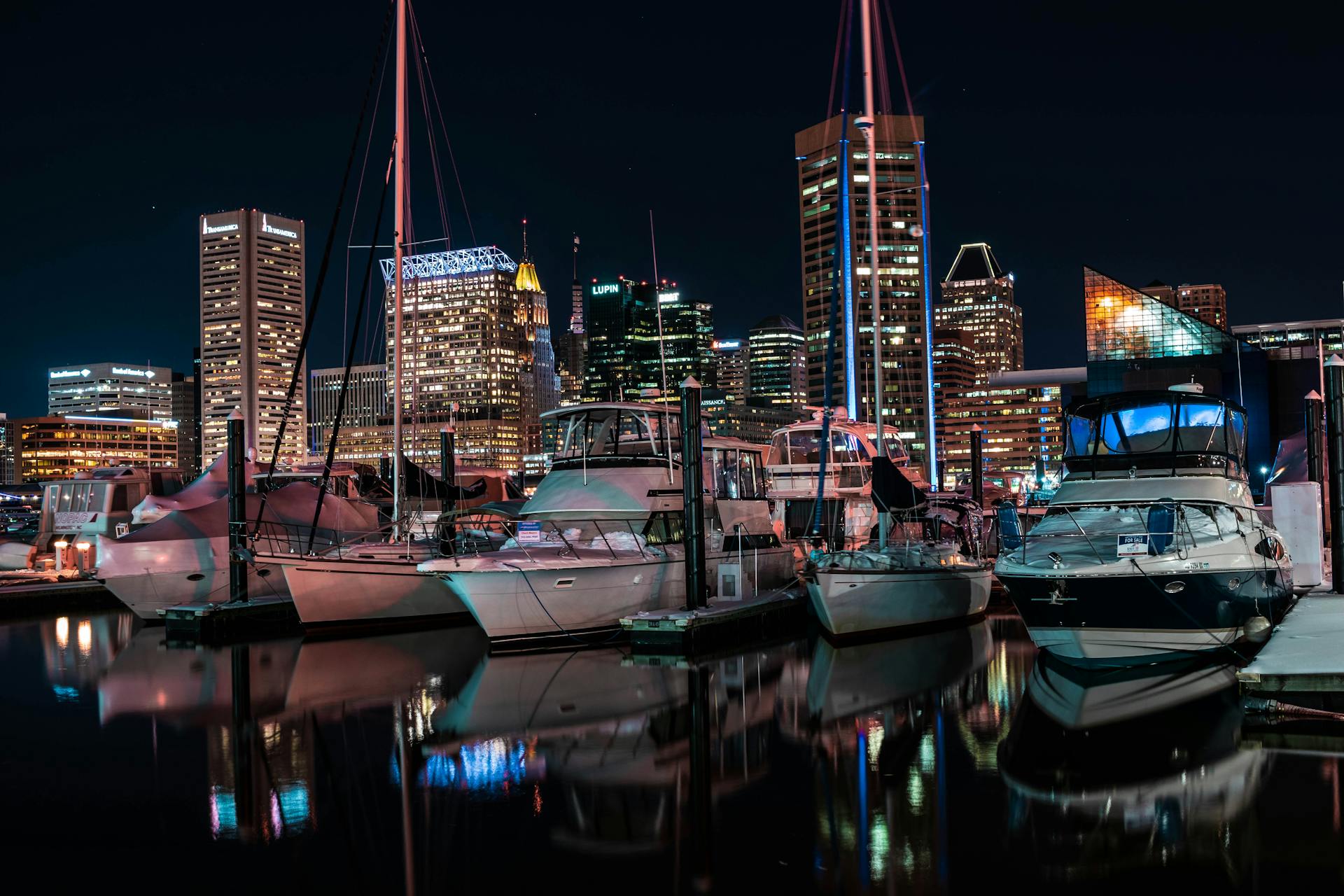 Baltimore skyline illuminated at night with yachts docked in the marina, reflecting urban luxury.