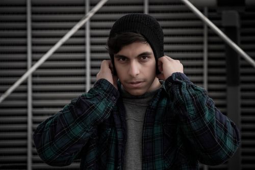 Free Portrait of a young adult man wearing a beanie and plaid shirt, posing with a serious expression outdoors. Stock Photo