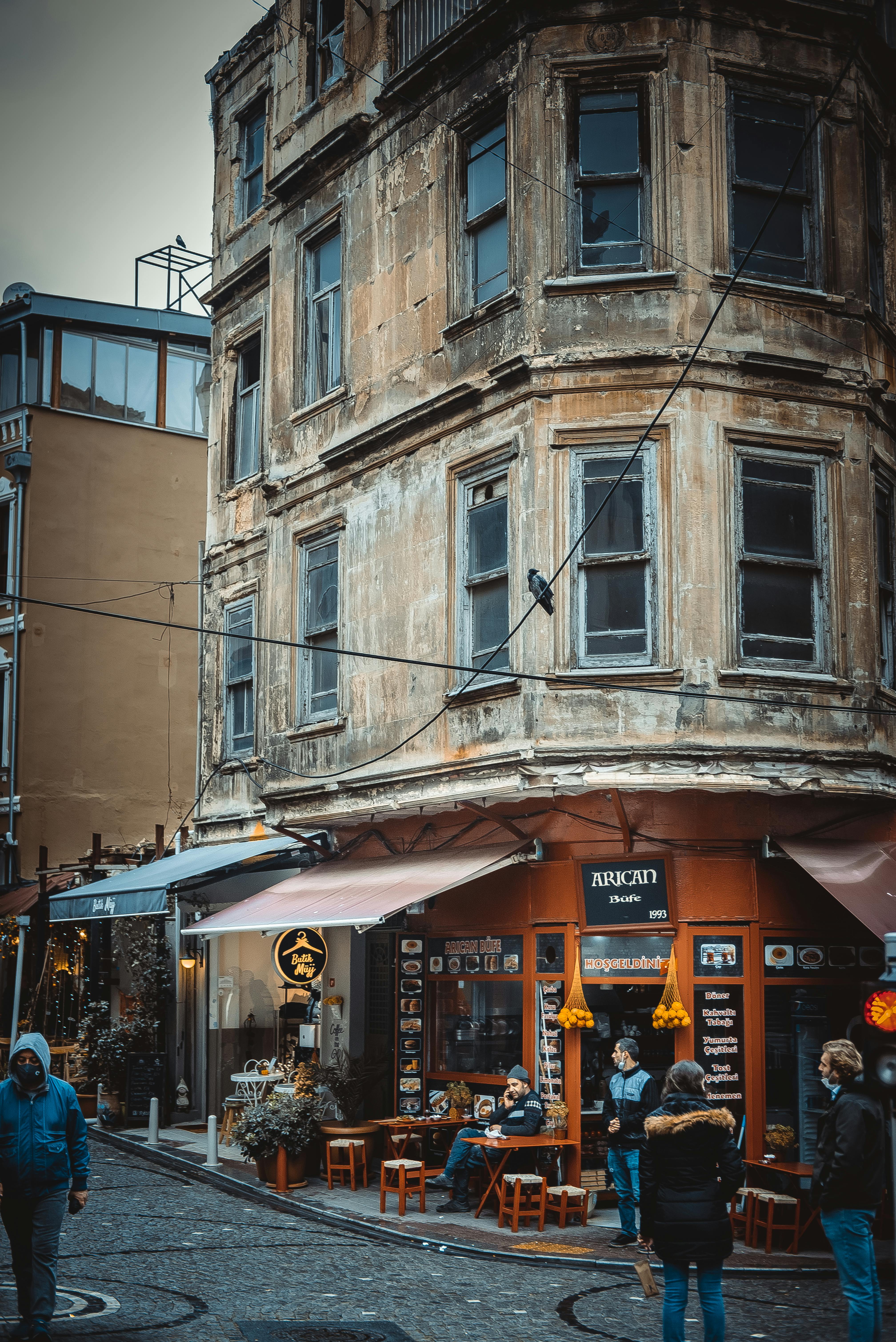 Free Vintage building on a busy city street corner with pedestrians and a cozy café vibe. Stock Photo