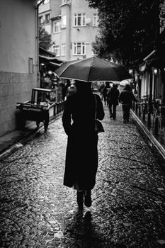 Silhouette of a woman with umbrella walking on a rainy cobblestone street in the city.
