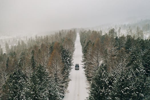A scenic aerial view of a car on a snowy forest road in Altai during winter.