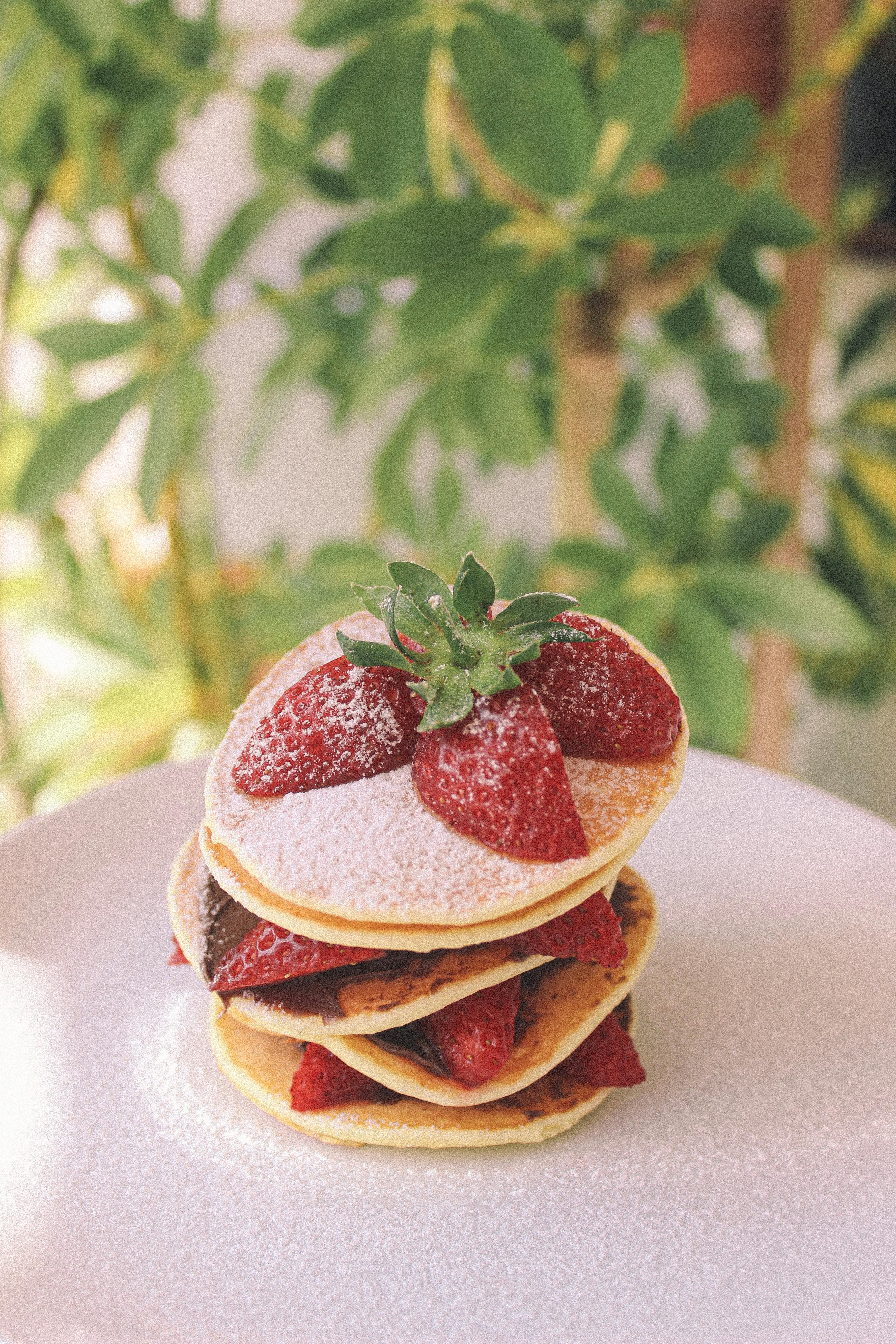 Stack of fluffy pancakes topped with fresh strawberries and powdered sugar, perfect for breakfast.