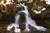 Tranquil waterfall cascading over mossy rocks in a snowy forest setting, perfect for nature enthusiasts.