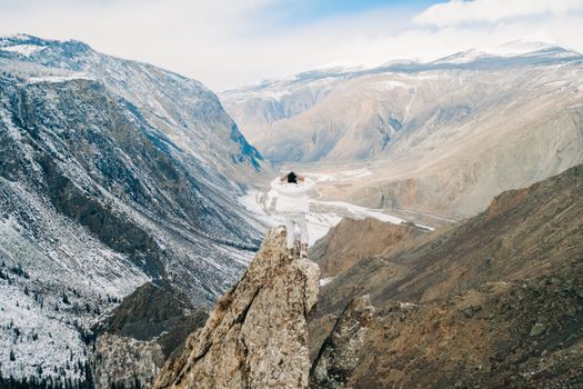 A person stands on a snowy cliff in Ulaganskiy Rayon, showcasing the vast landscape.