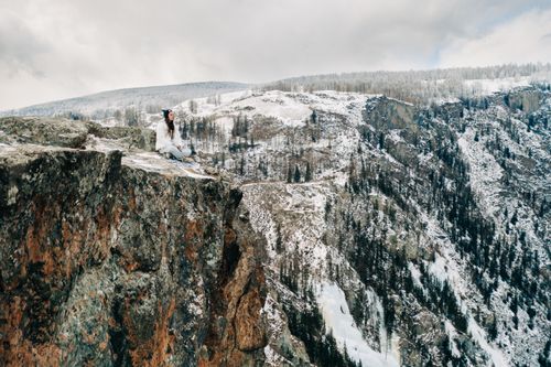 Free A woman sitting on the edge of a cliff overlooking snow-covered mountains in Altai, Russia. Stock Photo