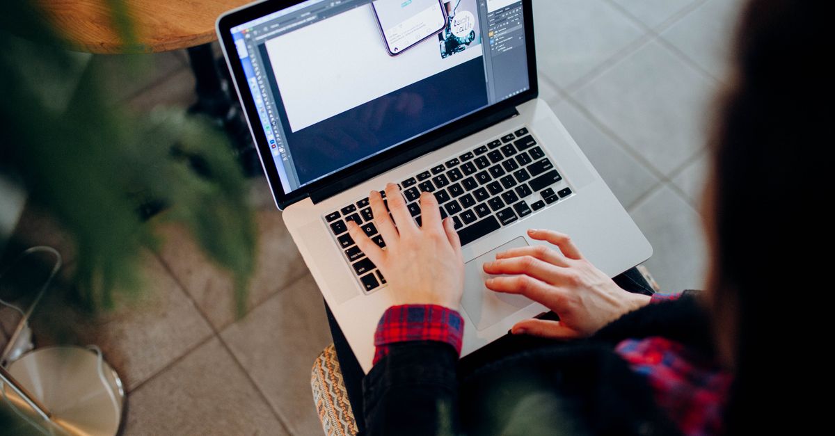 High-angle shot of a person using a laptop with design software, indoors on a tiled floor.
