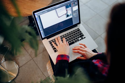 High-angle shot of a person using a laptop with design software, indoors on a tiled floor.