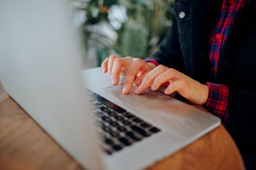 Close-up of hands typing on a laptop at a wooden desk surrounded by plants. Ideal for remote work themes.