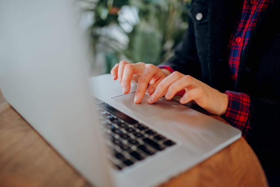 Does QuickBooks Self-Employed Help Track Write-Offs? Close-up of hands typing on a laptop at a wooden desk surrounded by plants. Ideal for remote work themes.