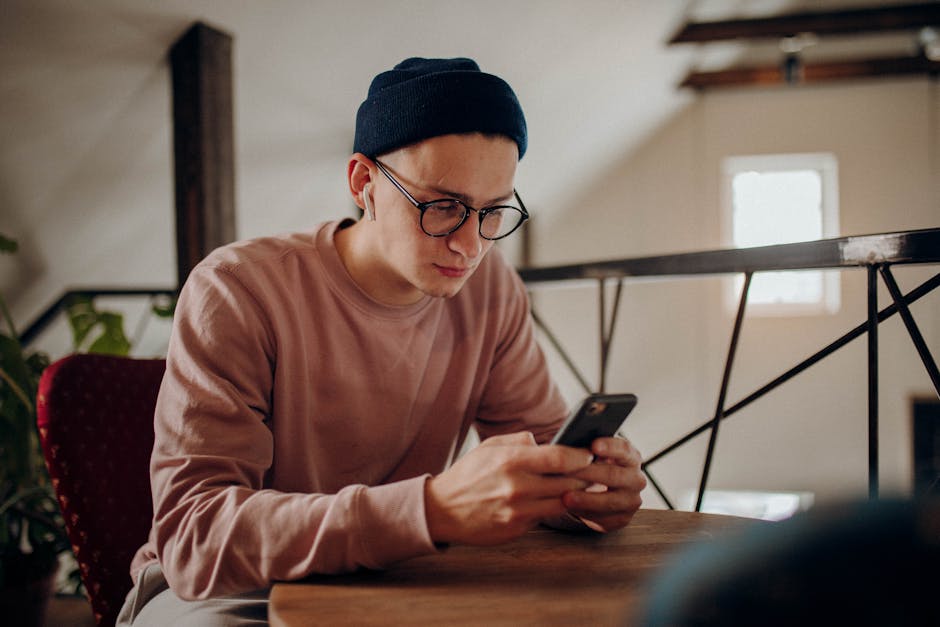 Casual young man with glasses using smartphone in trendy indoor setting.