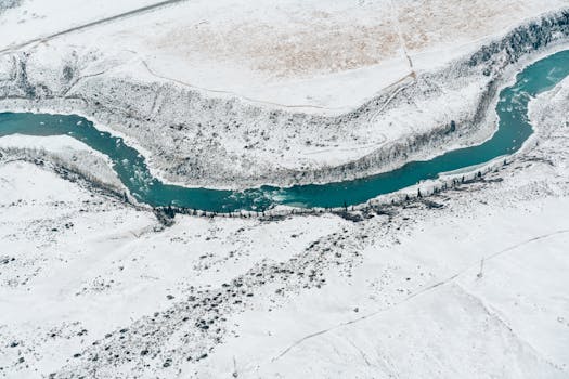 Stunning aerial view of a meandering river cutting through a snow-covered terrain, captured by drone.