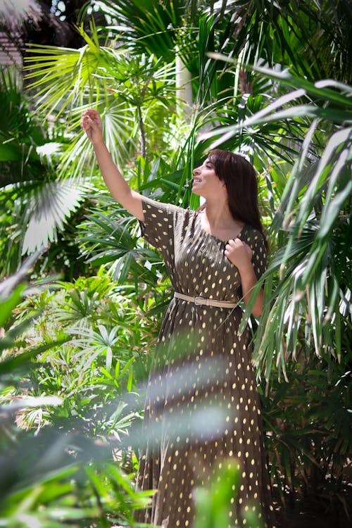 Free A Woman in Brown Dress Standing while Reaching Green Leaves Stock Photo
