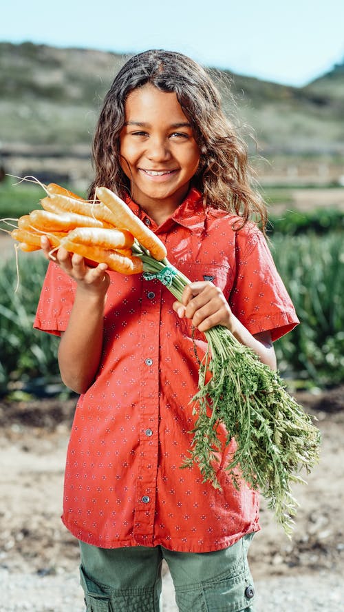 A Young Boy Holding a Bunch of Fresh Carrots