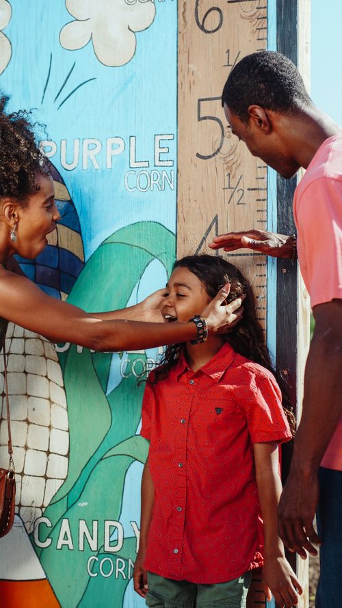 Free Joyful family measuring their child at a colorful amusement park attraction. Stock Photo