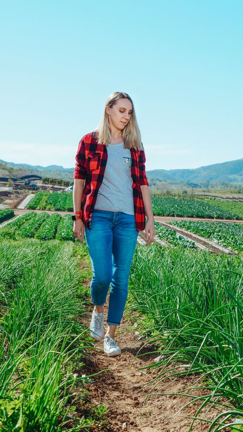 Free A young woman in casual attire walks through a lush farm field on a sunny day. Stock Photo