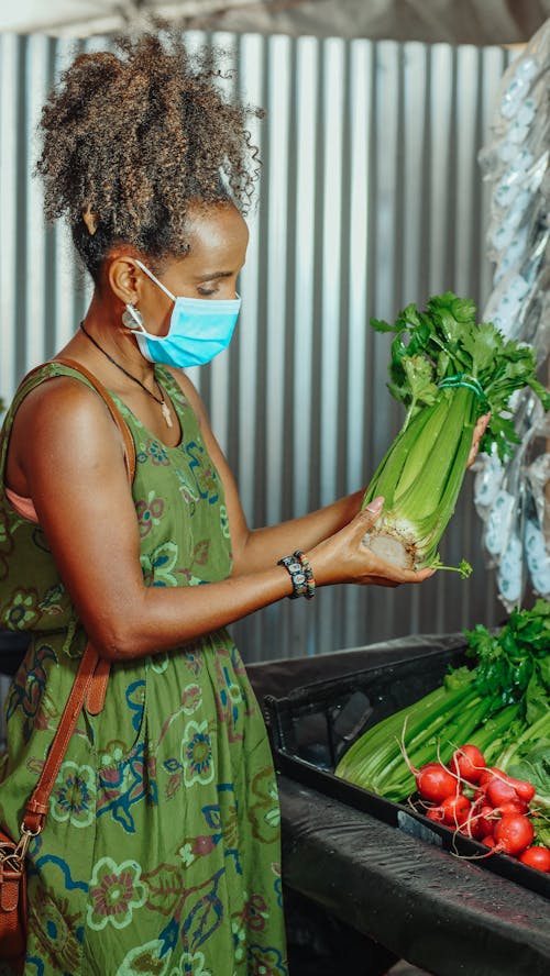 Woman in Green Dress With Facemask Holding Vegetable on Market 