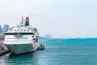 在清澈的蓝色海水和城市天际线的背景下，一艘豪华游轮停靠在繁忙的港口