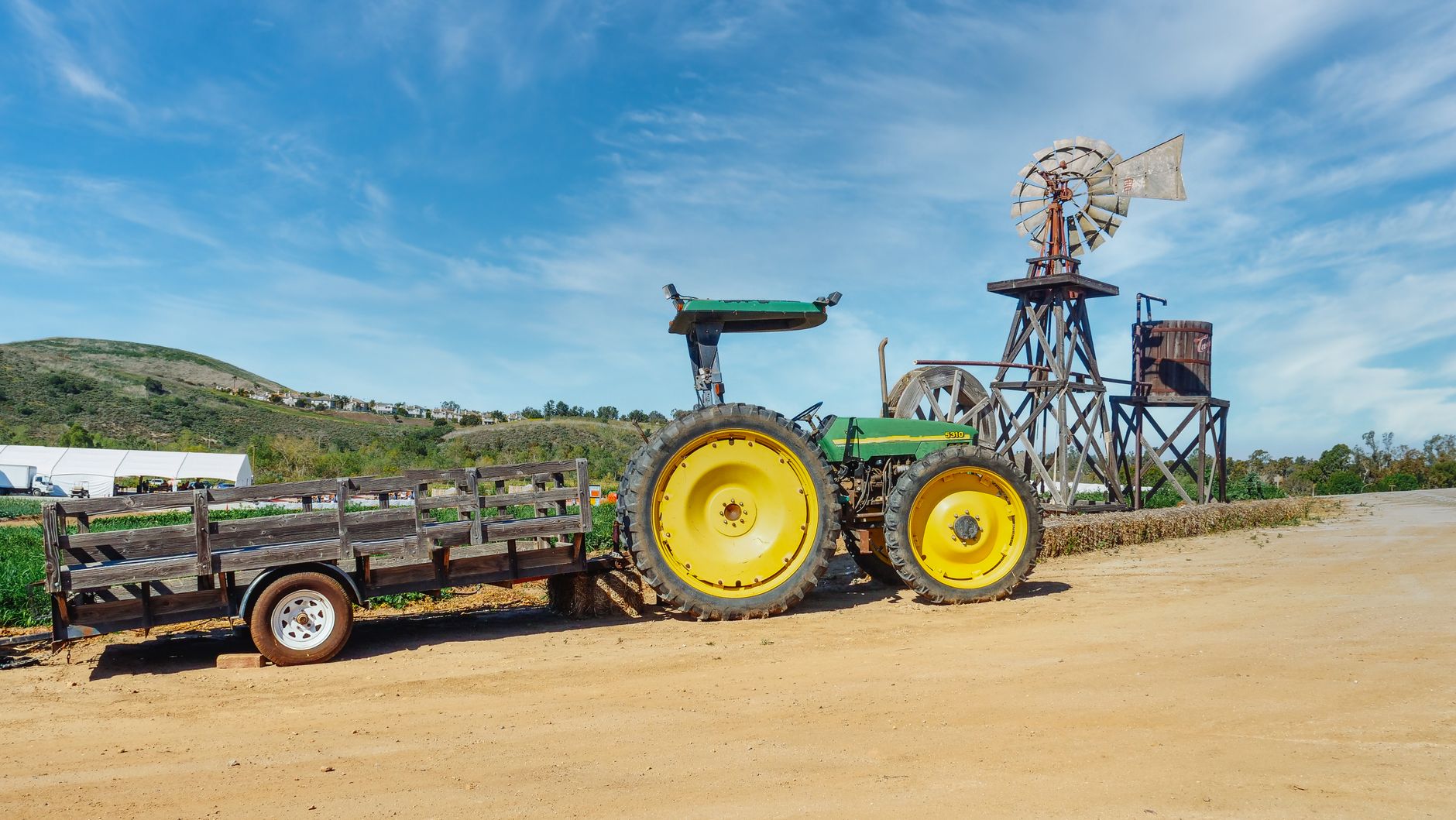A rustic landscape featuring a tractor and windmill on a sunny day at a farm.
