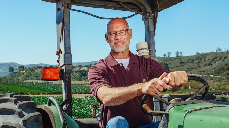 Elderly Man In Maroon Polo Shirt Driving A Tractor