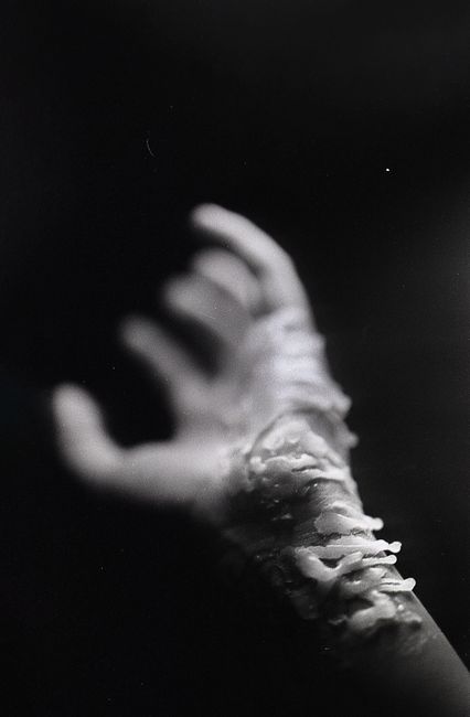 Black and white of crop anonymous person with candle wax on hand against dark background