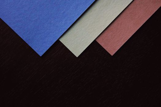A composition of blue, gray, and red triangular papers on a textured black surface, showcasing geometric design.
